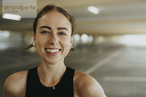 Portrait of happy young woman in black sleeveless casual at parking garage