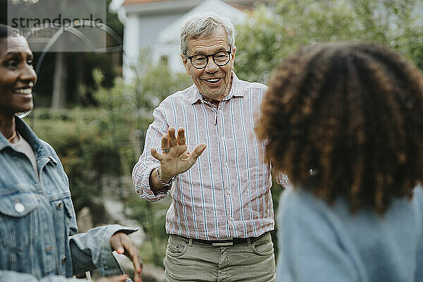 Smiling senior man wearing eyeglasses and greeting friends in garden party