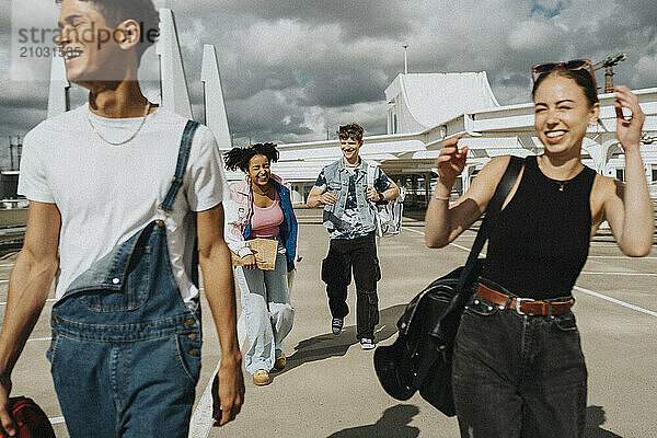 Happy male and female friends having fun while walking at parking lot on sunny day