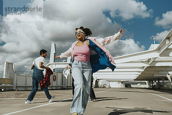 Carefree fashionable young woman dancing in parking lot under cloudy sky