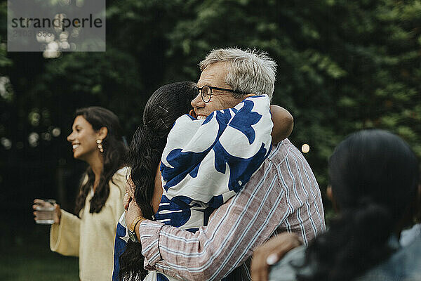 Happy senior man hugging female family member during social gathering in back yard