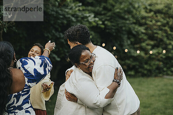 Happy senior woman hugging male family member during social gathering in back yard