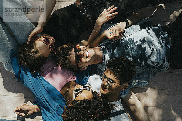 High angle view of cheerful young male and female friends lying down on floor in sunlight