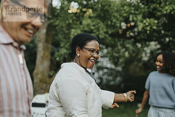 Carefree active senior woman dancing with family members during social gathering at garden party