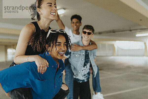 Happy curly hair young woman piggybacking female friend in parking garage