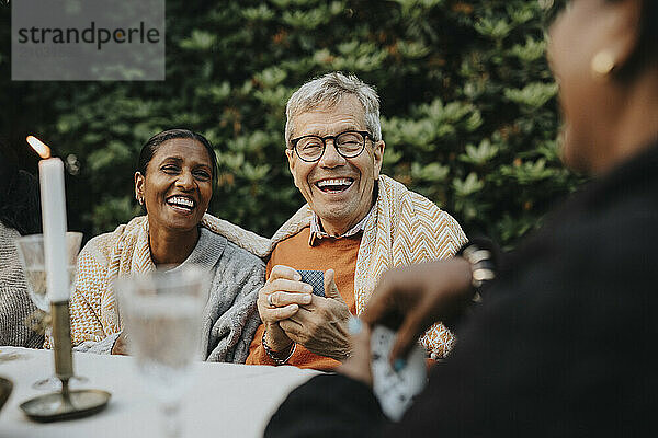 Cheerful senior man playing cards with family members at garden party