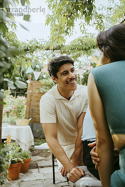 Smiling young man talking with woman sitting in back yard at dinner party