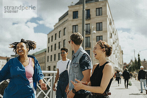 Cheerful young woman having fun with male and female friends while walking on street