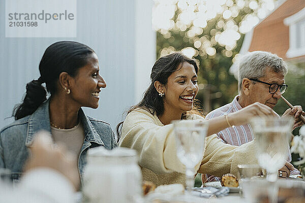 Cheerful teenage girl having lunch with family members during social gathering at garden party