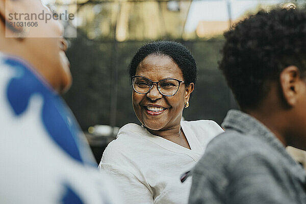 Happy senior woman with eyeglasses talking with female family friend during social gathering