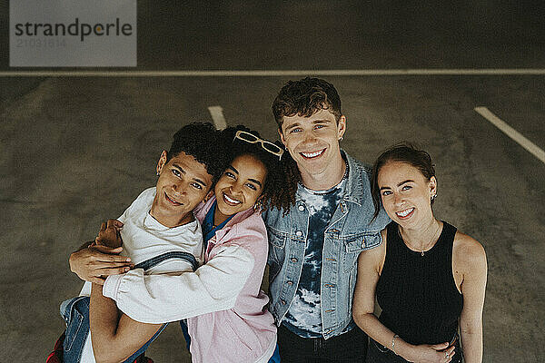 High angle portrait of cheerful male and female friends standing side by side in parking garage