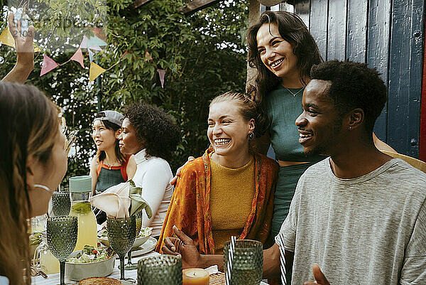 Happy male and female multiracial friends talking while celebrating in back yard during dinner party