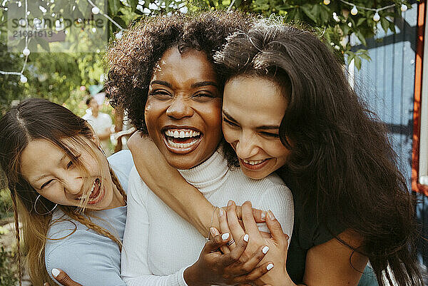 Cheerful female friends embracing each other while laughing at dinner party