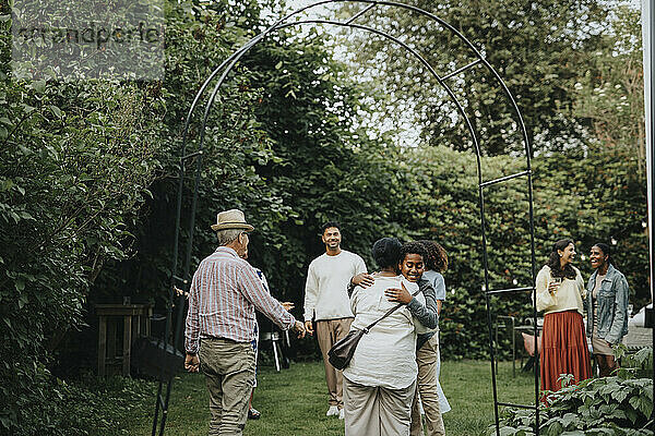 Happy male and female family members welcoming grandparents during social gathering at garden party