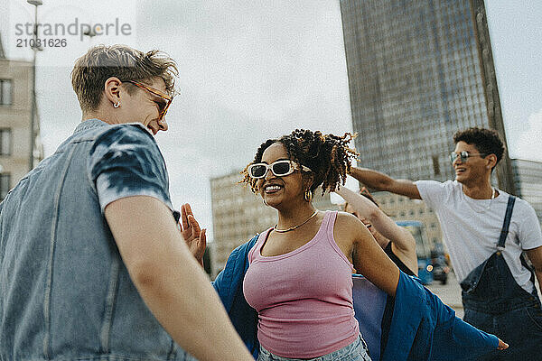 Cheerful curly hair woman in sunglasses dancing with male friend on street