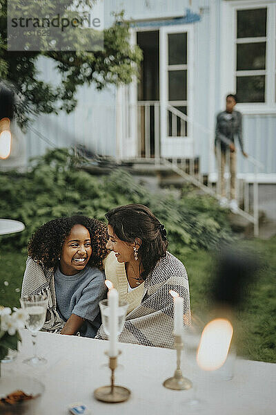 High angle view of teenage girl with arm around female friend sitting near table and discussing at family gathering