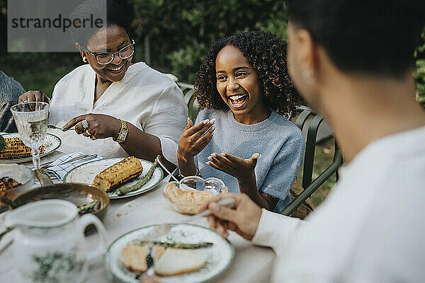 High angle view of cheerful girl discussing with family members at lunch during social gathering