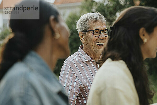 Cheerful senior man enjoying social gathering with friends at garden party