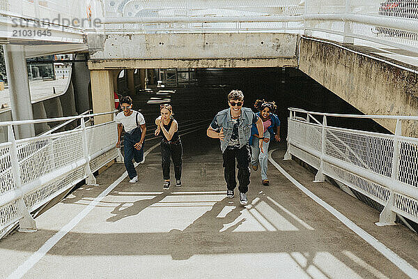 Playful male and female friends running on footpath of parking garage at sunny day