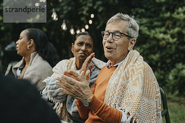 Senior man clapping and enjoying with family members during social gathering at garden party