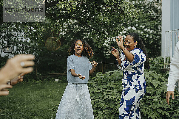 Carefree mother and daughter dancing with family members in back yard