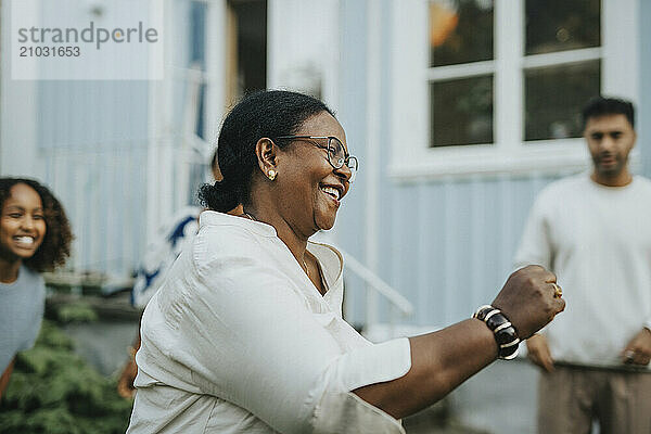 Carefree senior woman dancing with family members in back yard