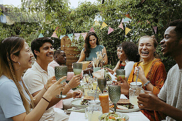 Happy group of male and female friends enjoying drinks while celebrating at dinner party