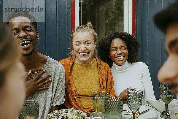 Happy male and female friends laughing while having fun at dinner party in back yard