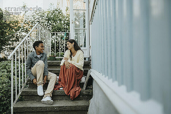 Happy boy talking with female cousin and sitting on steps outside house