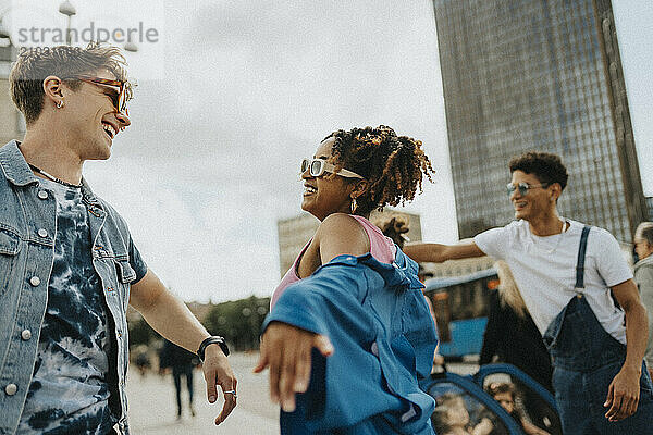 Carefree curly hair woman in sunglasses dancing with male friend on street