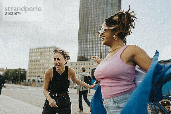 Cheerful young female friends enjoying while dancing on street under clear sky