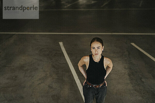 High angle view of young woman in black casuals standing with hands on hip at parking garage