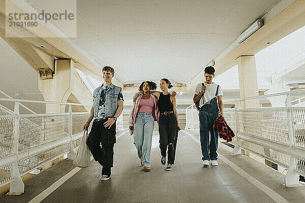 Happy young fashionable male and female friends walking on footpath of parking garage