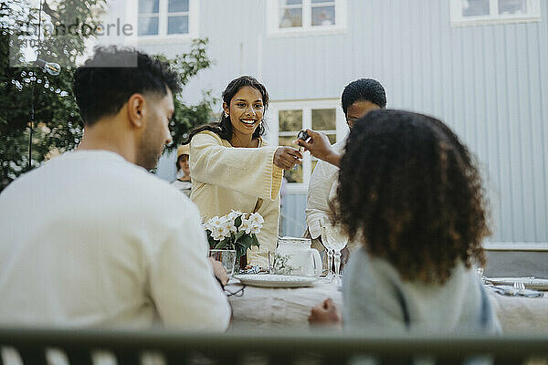 Smiling woman passing spoon to female friend during dinner party in garden