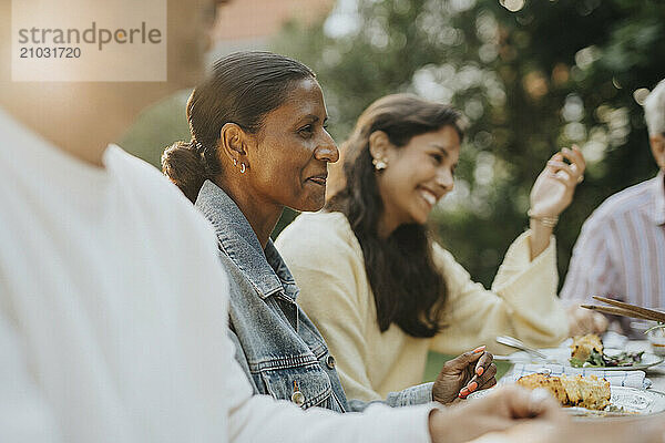 Smiling mature woman having lunch with family members during social gathering