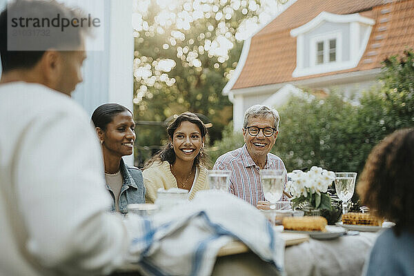 Happy senior man having lunch with family members during social gathering at garden party