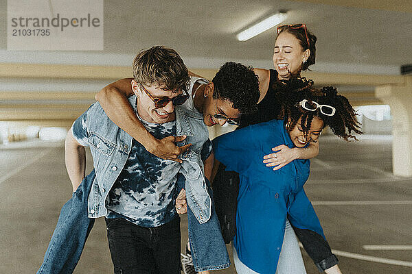 Playful young man and woman piggybacking friends in parking garage