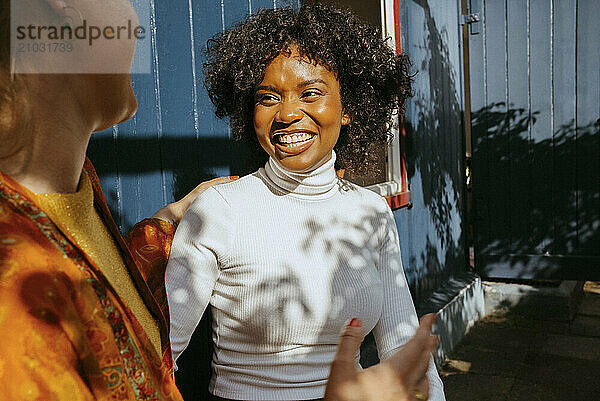 Happy young woman in turtleneck talking with female friend at dinner party