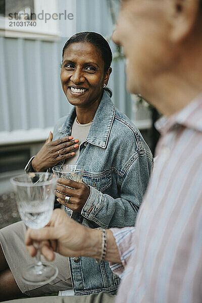 Cheerful woman holding glass while discussing with senior family member during garden party