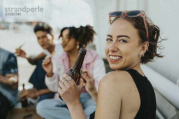 Portrait of beautiful young woman holding beer bottle while looking over shoulder at parking lot