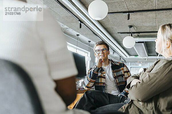 Male tech entrepreneur with hand on chin talking with colleagues in office