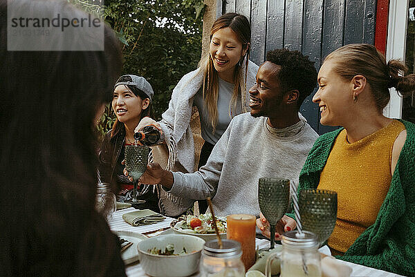 Smiling woman pouring drink in glass of male friend sitting at dining table during party