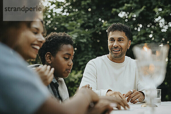 Mature man sitting with family members during social gathering at garden party