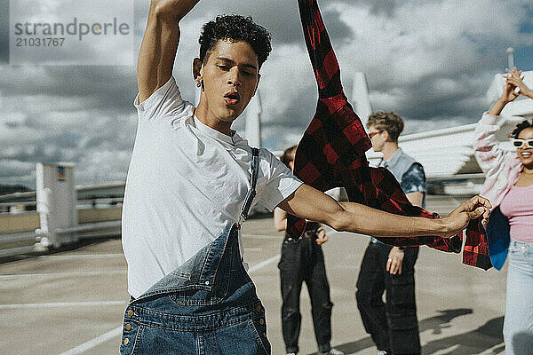 Carefree young man holding jacket and dancing with friends in parking lot