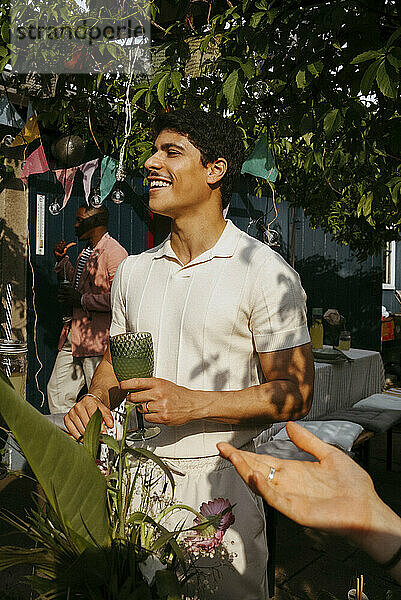 Smiling young man holding drink glass while having fun at dinner party