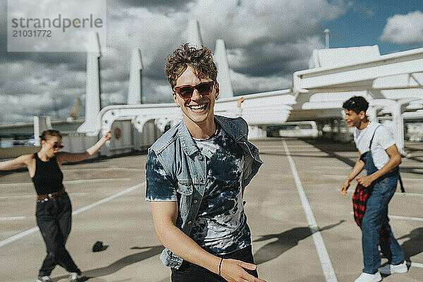 Portrait of carefree fashionable young man enjoying with male and female friends in parking lot under cloudy sky