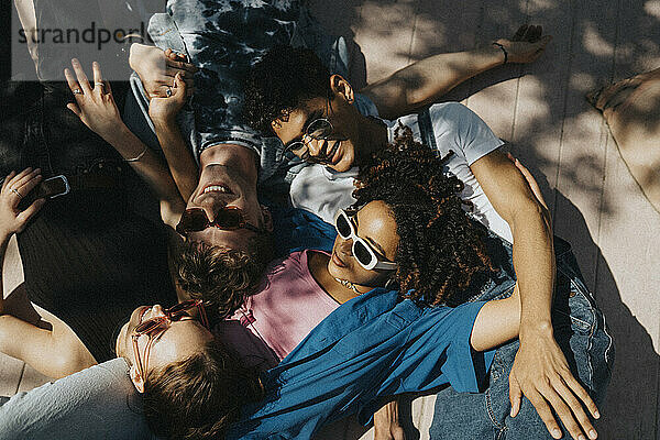 High angle view of fashionable young male and female friends lying down on floor in sunlight