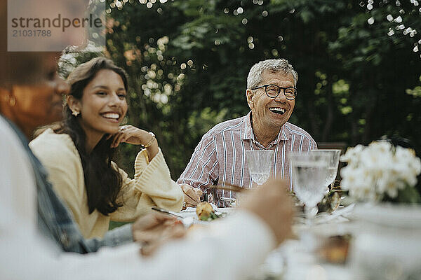 Happy senior man enjoying and having fun with family members at lunch party