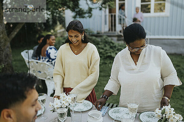 Female family members setting table for dinner during social gathering at garden party