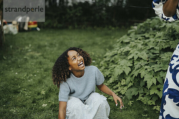 Happy girl crouching near plants in back yard